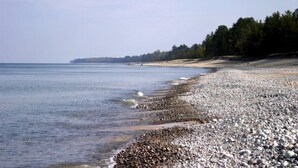 Une plage de galets, une mer calme, une ligne d’arbres à l’horizon et un ciel dégagé.