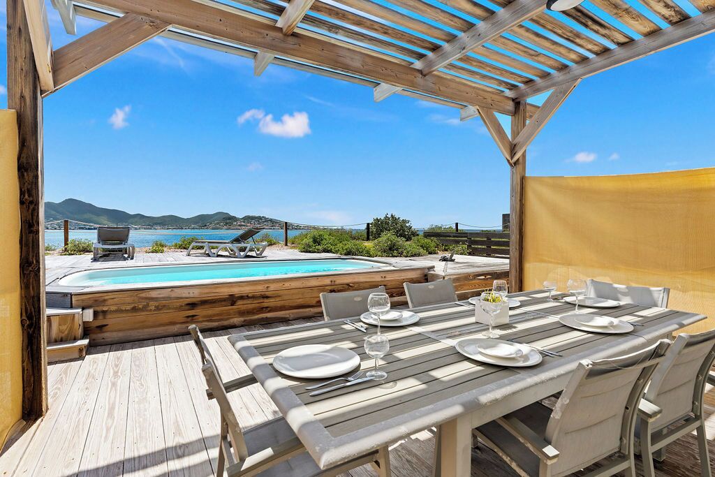 Une terrasse en bois avec une piscine, un espace repas extérieur et une vue sur la mer et les montagnes.