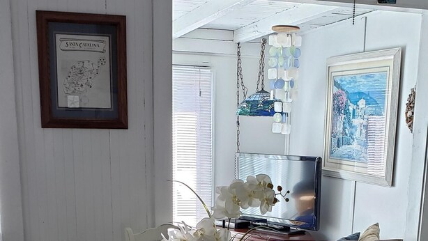 A dining area with a glass table, white chairs, and a vase of white flowers.