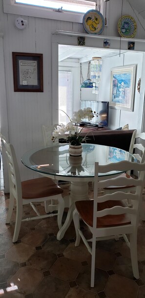 Un comedor con una mesa de vidrio, sillas blancas y un jarrón con flores blancas.