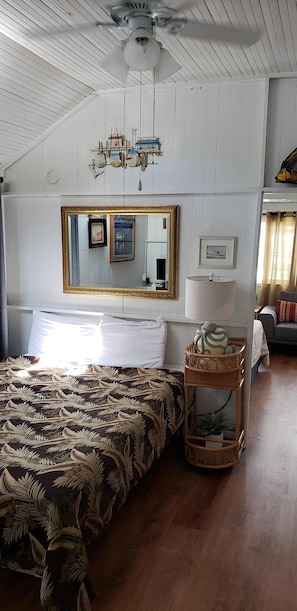 Cozy retreat with a large bed, ceiling fan, and mirror above, plus a bedside table with a lamp and decorative item.