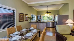 A dining area with a table set for four, a kitchen in the background, and a ceiling fan. - Aloha Villa: AC, Garden, Short Walk to Poipu Beach (Koloa)