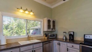 A kitchen with a window, sink, cabinets, a toaster, and a coffee maker. - Aloha Villa: AC, Garden, Short Walk to Poipu Beach (Koloa)
