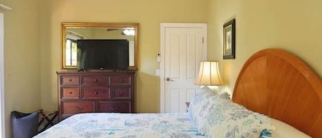 Une chambre à coucher avec un lit, une commode, un miroir, une porte et une lampe.