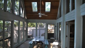 A covered patio with a table and chairs, large windows, and a ceiling fan.