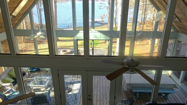 A room with a view of a lake, a ceiling fan, and a wooden deck outside.