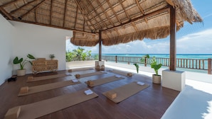 Una sala yoga con tappetini e supporti, un tetto di paglia e vista sull'oceano.