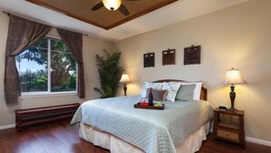 Un dormitorio con una cama, una mesita de noche, un ventilador de techo, una ventana con cortinas y adornos en la pared.