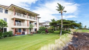 Un hotel de varios pisos con un balcón de dos niveles, un césped bien cuidado y jardines tropicales.