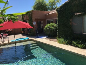Une piscine avec un parasol rouge, entourée d’un jardin et d’un bâtiment dont le toit est recouvert de tuiles.