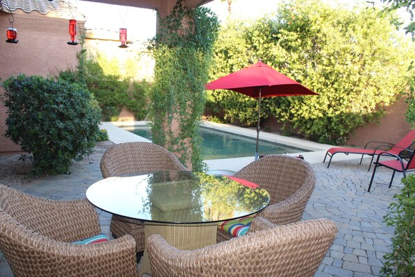 Une terrasse avec des meubles en osier, une table en verre et un parasol rouge.