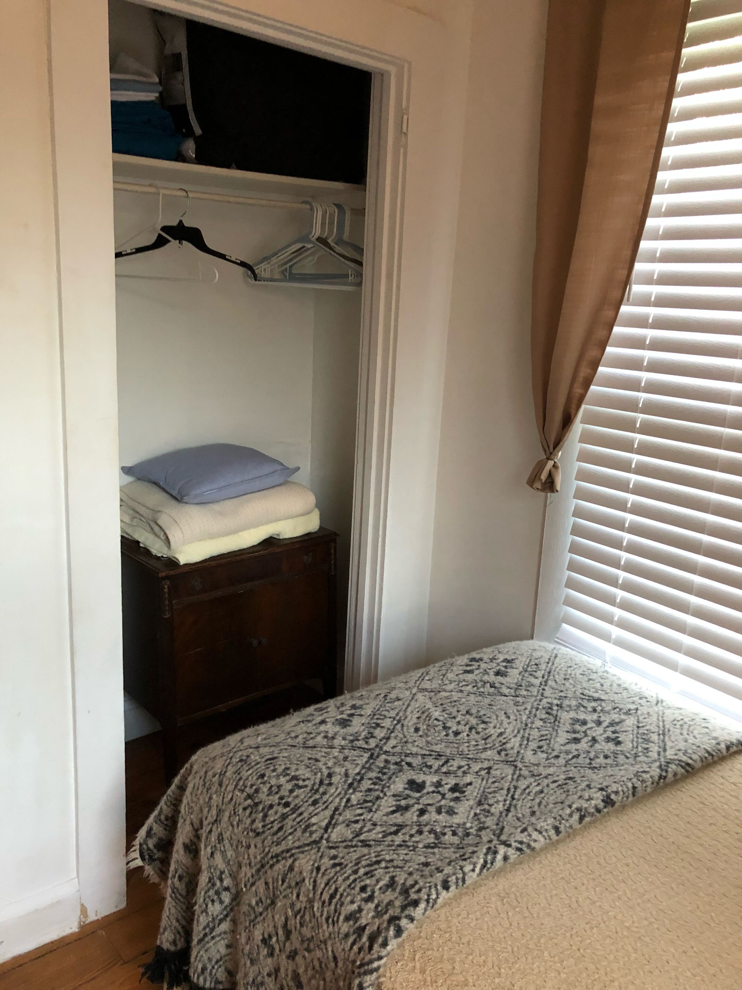 A bedroom with a bed, a wardrobe, and a window with blinds.