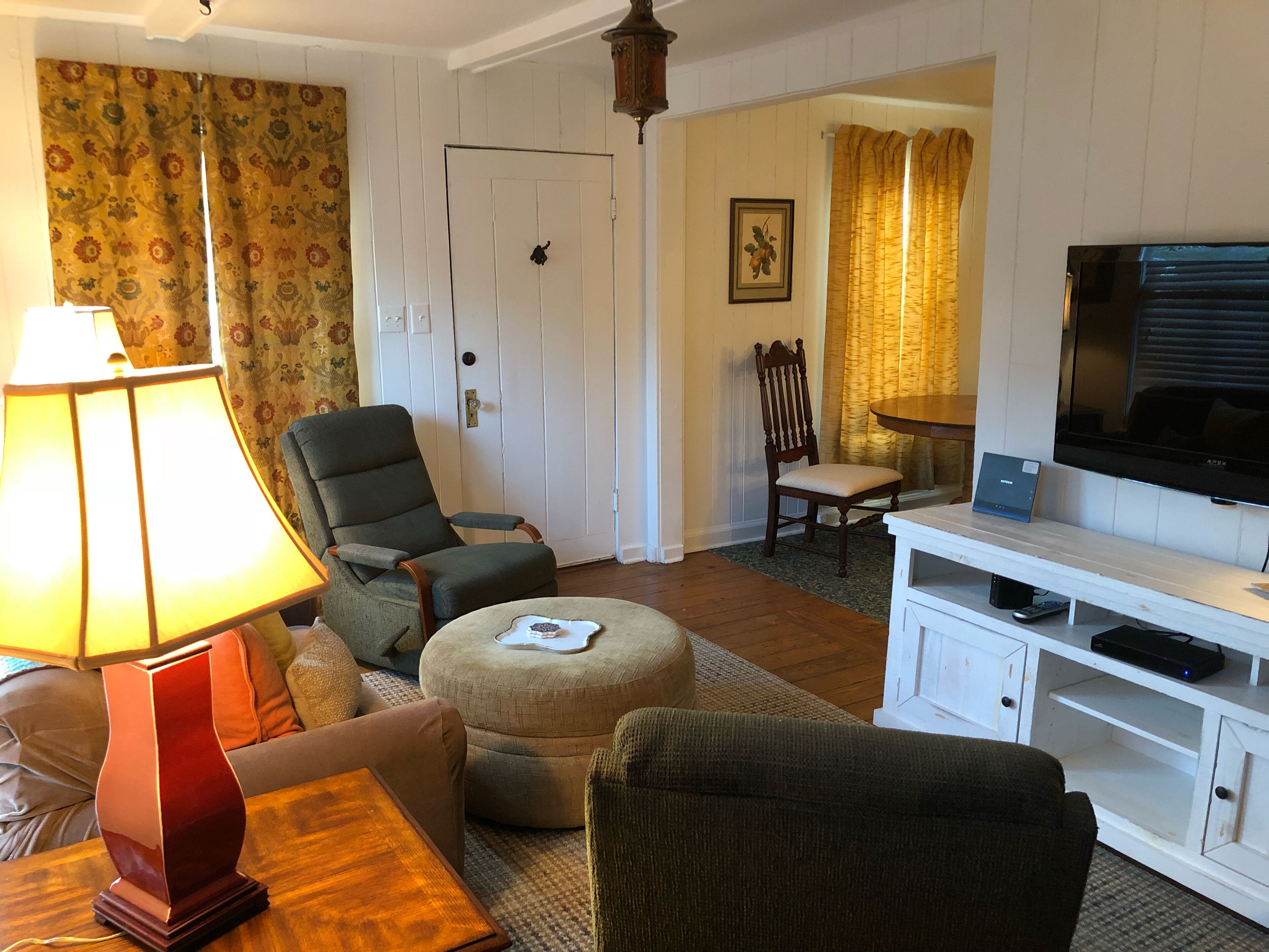Una sala de estar con sofá, sillón, reposapiés, televisor y lámpara.
