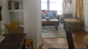 A living room with a white brick wall, a wooden dining table, a sofa, and a lamp. - Bungalow located in downtown Tryon, N.C.  (Tryon)