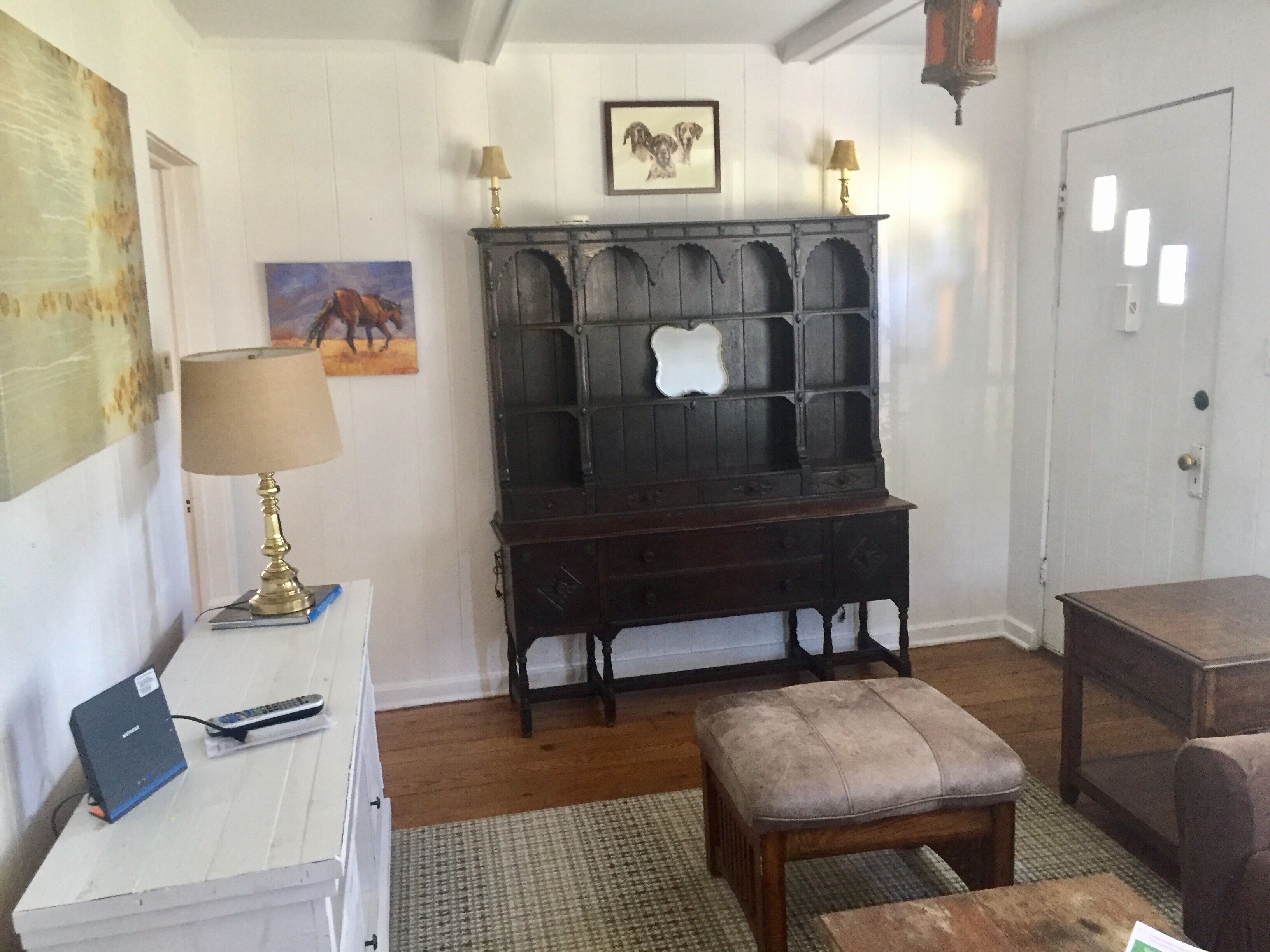 A room with a wooden bench, a desk with a lamp, a framed picture on the wall, and a door.