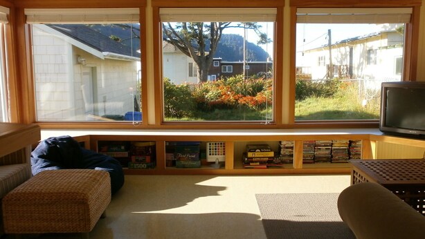 Een woonkamer met een groot raam, een bank, een televisie en een boekenkast met dvd's.