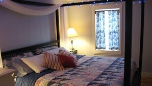 Een bed met een sprei, kussens, een bedlamp en een raam met gordijnen.