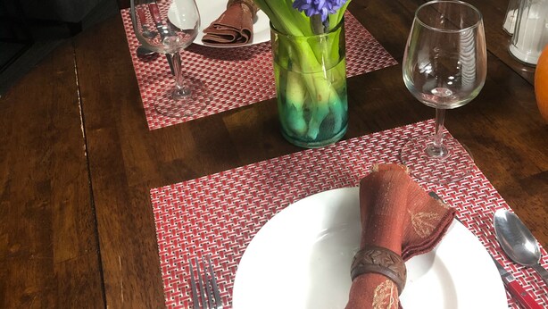 Ein Esstisch ist gedeckt mit einer Vase blauer Blumen, Tellern und Besteck.