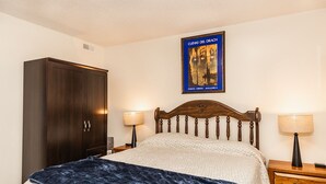 Un dormitorio con cama, armario de madera, dos mesitas de noche con lámparas y un cuadro en la pared.