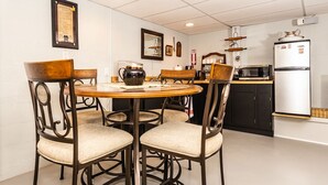 Un comedor con una mesa redonda y cuatro sillas, una zona de cocina con microondas y refrigerador, y un cuadro en la pared.