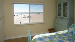 Quarto com uma grande janela com vista para a praia, cama com roupa de cama florida, armário azul e cesto de vime.