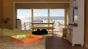 Sala de estar com uma grande janela com vista para a praia, um banco de madeira e uma televisão sobre um móvel.
