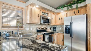 A kitchen with wooden cabinets, a stainless steel refrigerator, a microwave, a stove, and a sink.