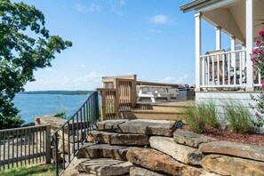 A coastal property with a stone staircase leading to a white porch with outdoor furniture.