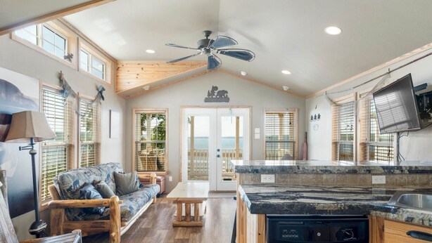 A spacious living area with a wooden ceiling, a sofa, a dining table, and a kitchen with a dishwasher.