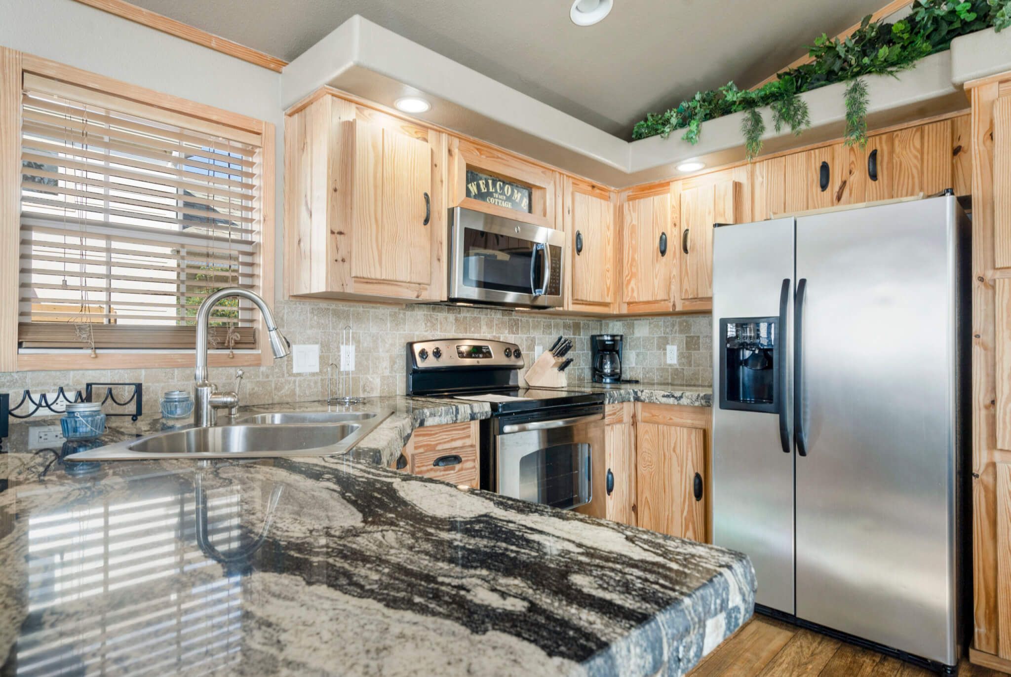 A kitchen with wooden cabinets, a stainless steel refrigerator, a microwave, a stove, and a sink.