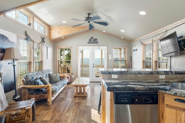 A spacious living area with a wooden ceiling, a sofa, a dining table, and a kitchen with a dishwasher.