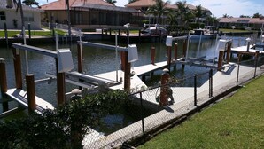 A marina with docked boats, a pedestrian walkway, and a residential area with houses in the background. - Beauty on the Water (Marco Island)