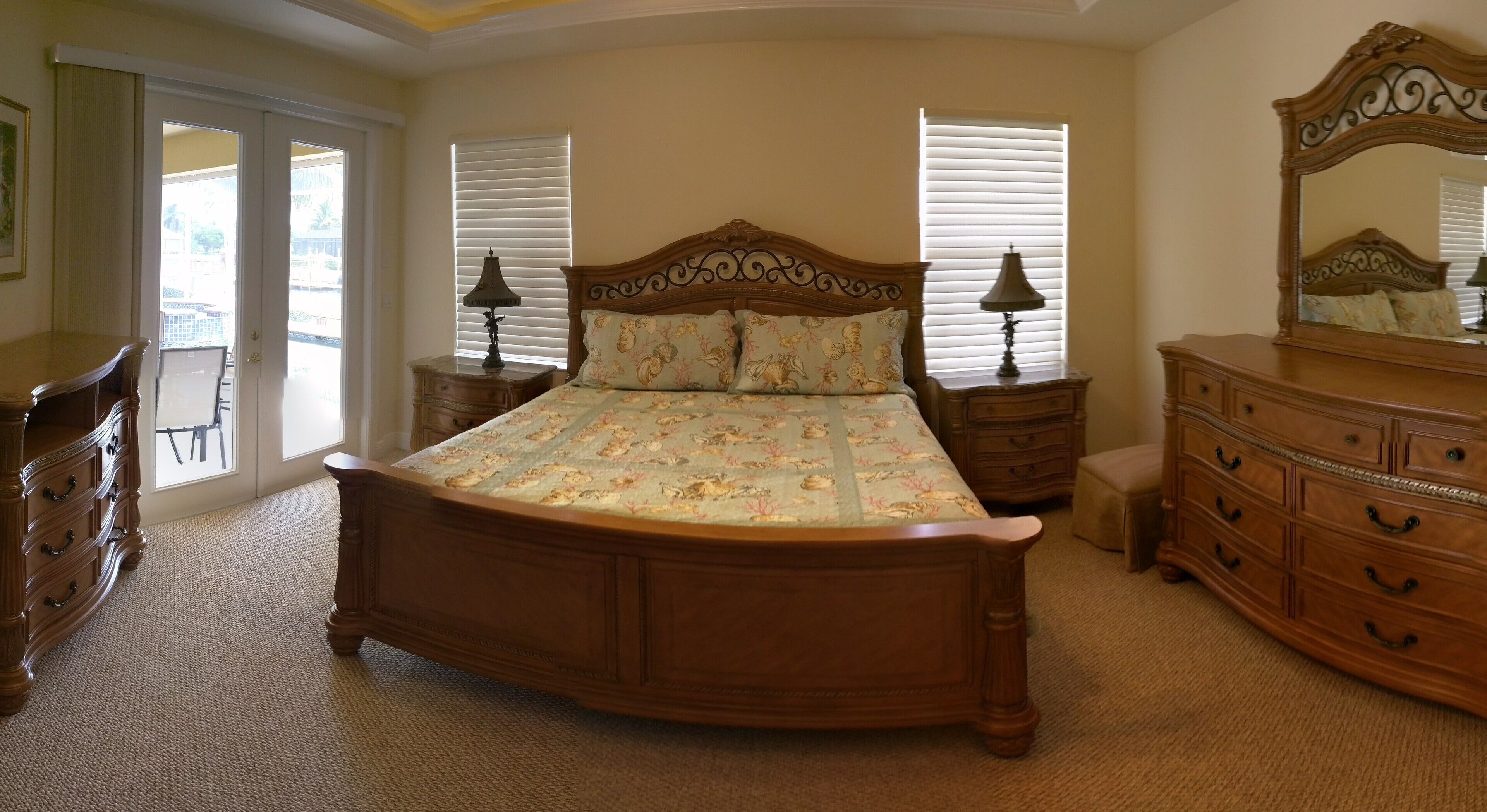 A bedroom with a large bed, two nightstands, a dresser, a mirror, and a chair.