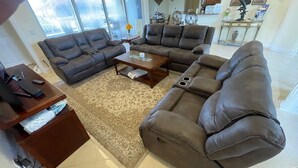 A living room with a brown leather sectional sofa, a glass coffee table, and a patterned rug. - Beauty on the Water (Marco Island)