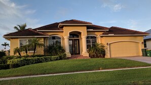 A two-story house with a brown tiled roof, beige walls, and a garage. - Beauty on the Water (Marco Island)