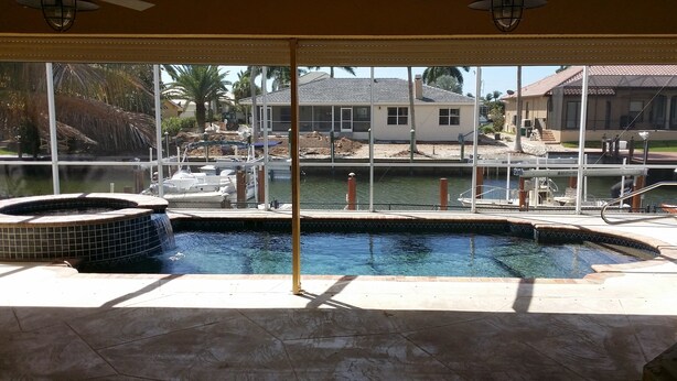 A swimming pool with a hot tub, surrounded by a covered patio area with a view of a house and docked boats. - Beauty on the Water (Marco Island)