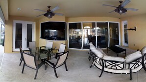 A covered patio area with a glass table and chairs, a ceiling fan, and a view through glass doors to the outside. - Beauty on the Water (Marco Island)