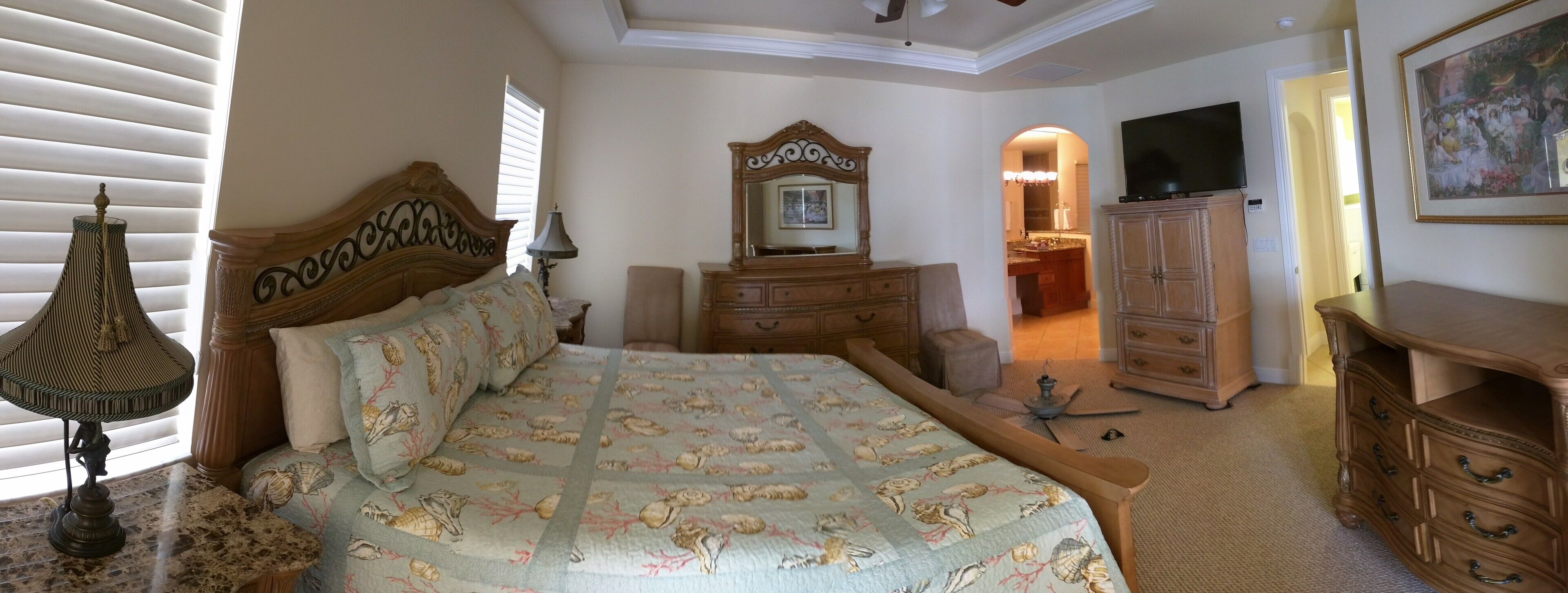 A bedroom with a bed, dresser, vanity, and a television.