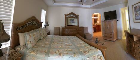 A bedroom with a bed, dresser, vanity, and a television.
