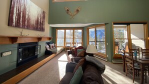 A cozy living room with a fireplace, large windows, and a view of the outdoors.