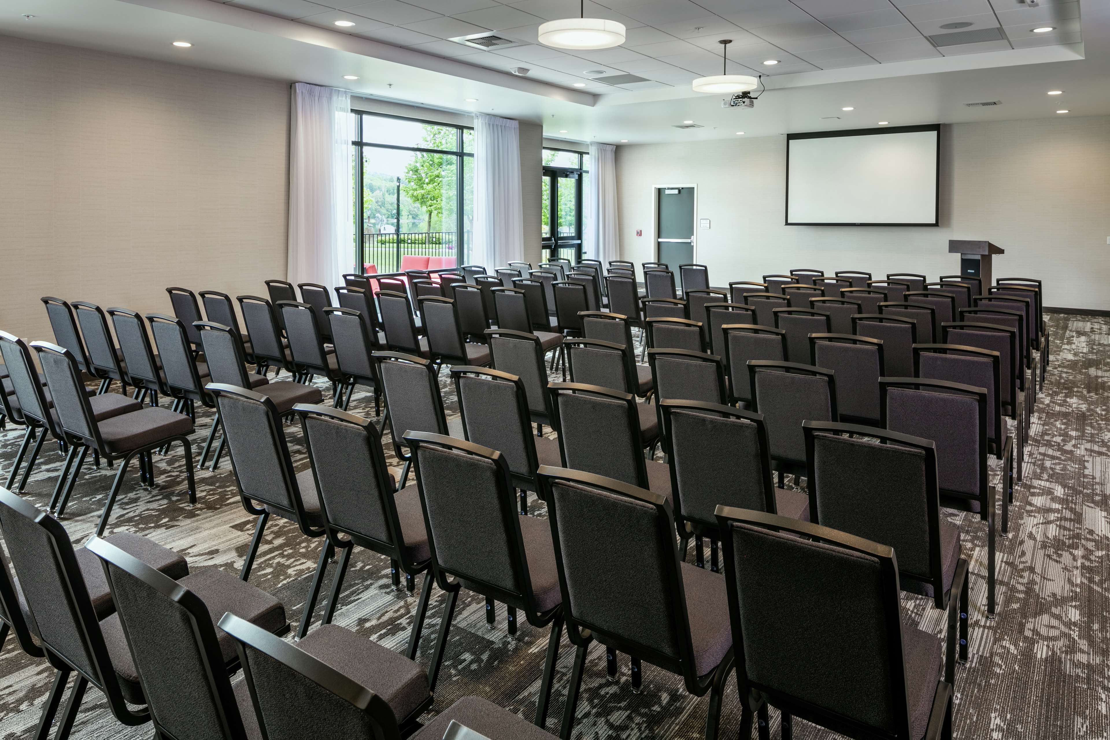 A conference room with rows of chairs, a projector screen, and a carpeted floor.