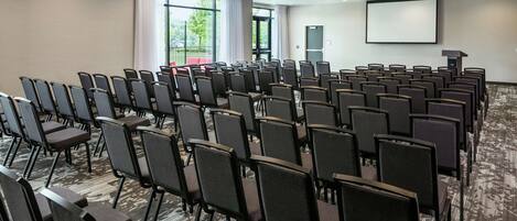 A conference room with rows of chairs, a projector screen, and a carpeted floor.