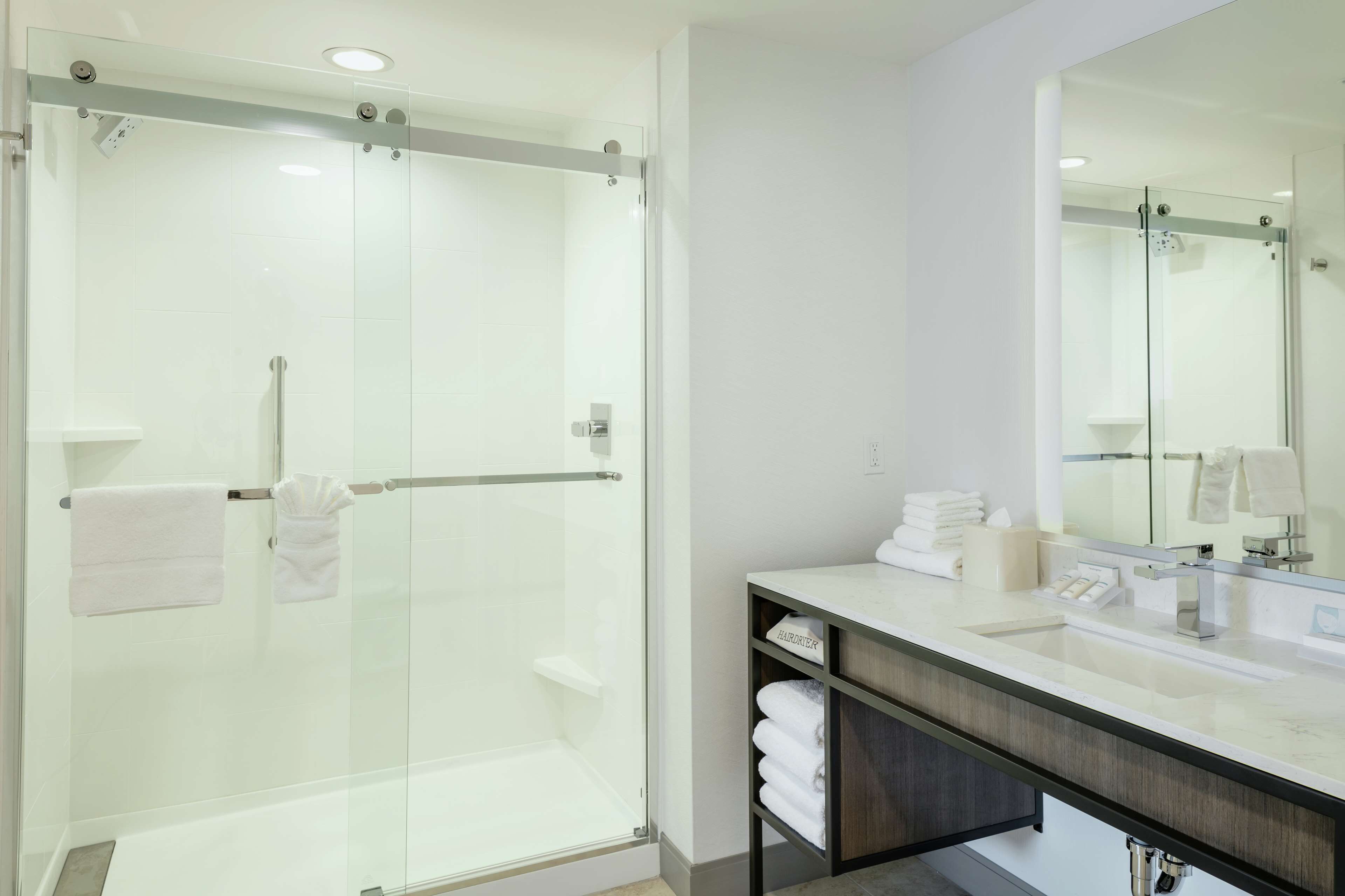 Un baño moderno con ducha envuelta en vidrio, tocador con espejo y toallas ordenadamente dobladas.