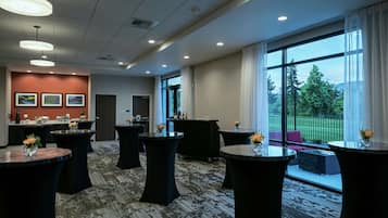 Ein moderner Konferenzraum mit runden Tischen, einer Rezeption und großen Fenstern mit Blick auf Grünflächen.