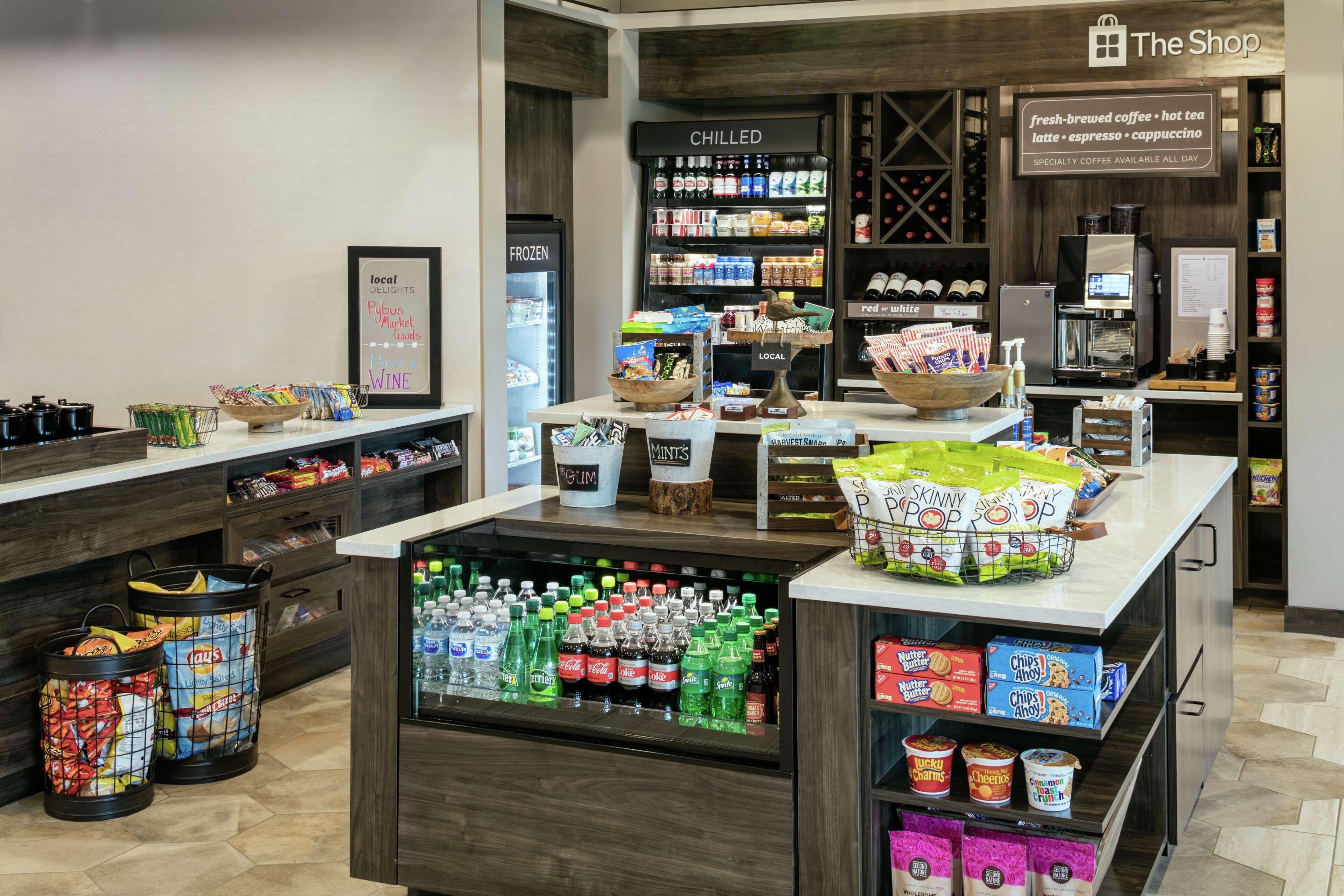 Interior de una cafetería con mostrador refrigerado, productos de snack y diversas bebidas.