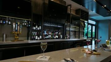A bar area with a variety of bottles and glasses, a pizza on a wooden board, and a wine glass on the counter.