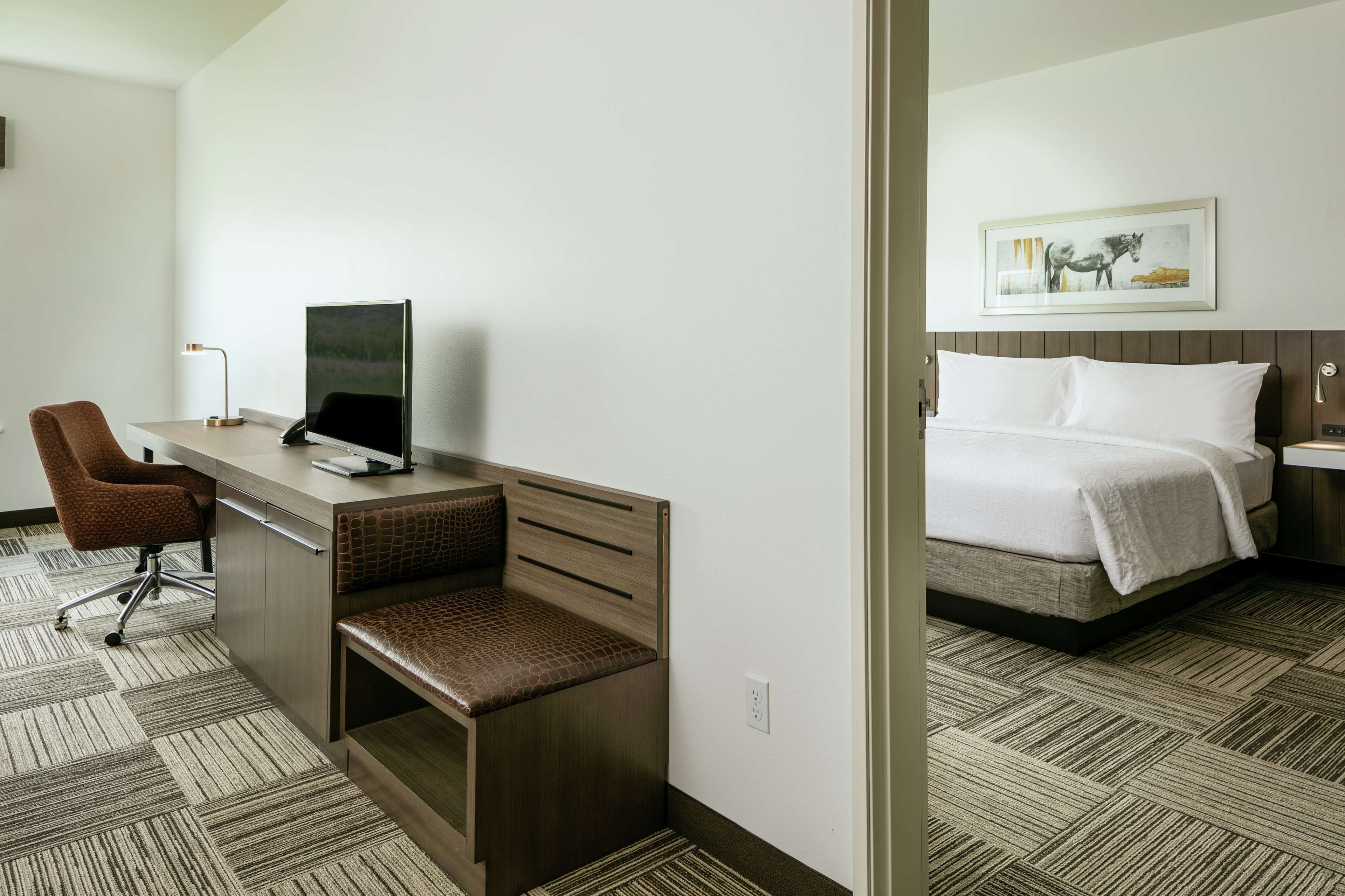 A hotel room with a desk, chair, and a bed.