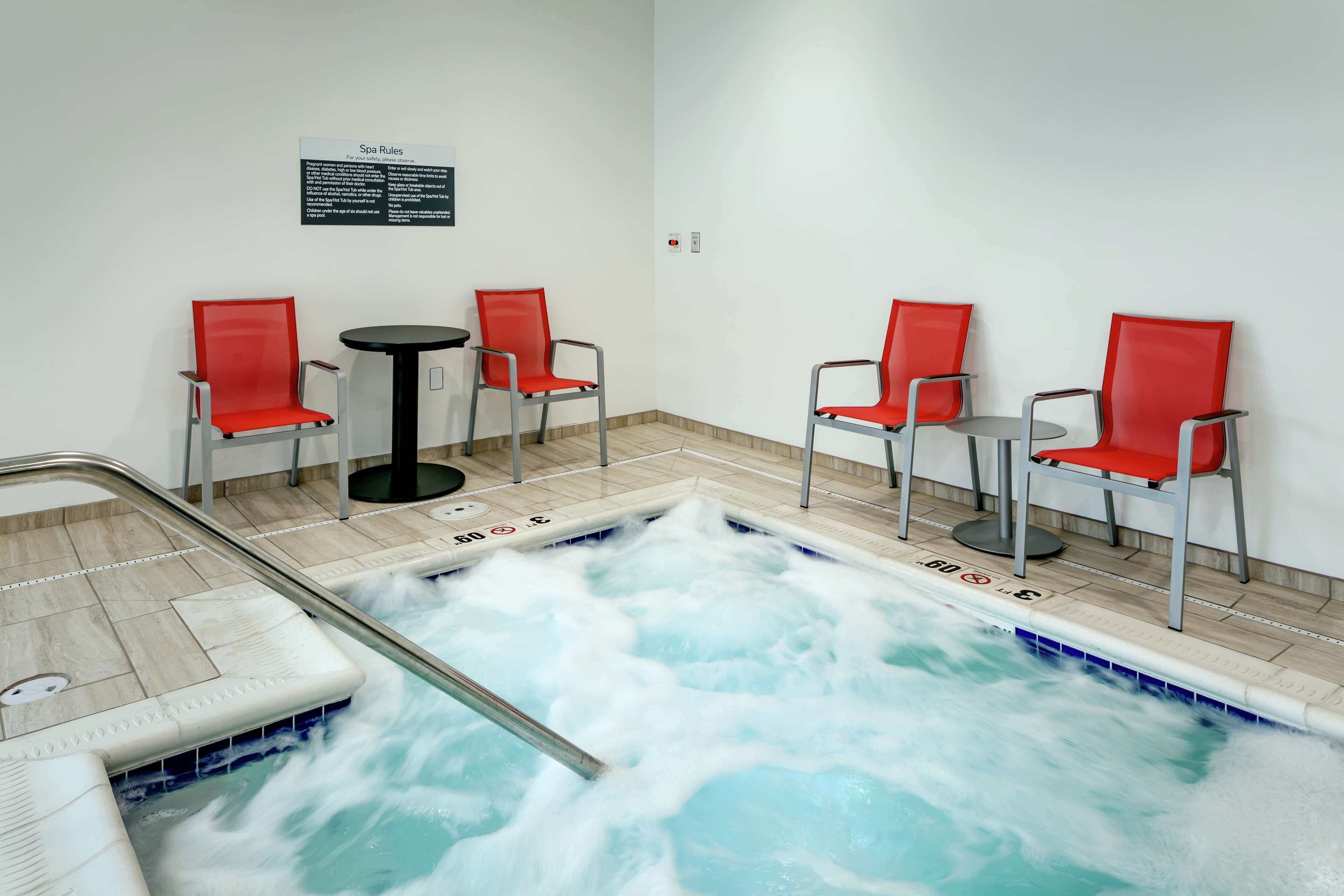 Ein Wellnessbereich mit Whirlpool, roten Liegestühlen, einem kleinen Tisch und einem Schild mit Spa-Regeln.