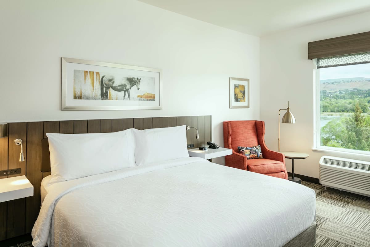 A hotel room with a large bed, a desk with a lamp, a chair, and a window with a view.