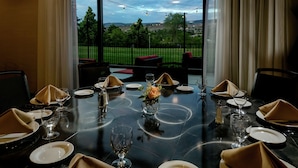 Une table à manger dressée pour quatre personnes, avec vue sur un paysage verdoyant grâce à de grandes fenêtres.